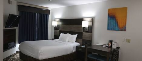 A hotel room with a large bed, a desk with a chair, a television, and a painting on the wall.