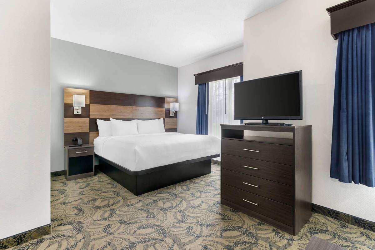 Une chambre d’hôtel avec un grand lit, un téléviseur posé sur une commode, une table de chevet et une moquette à motifs.