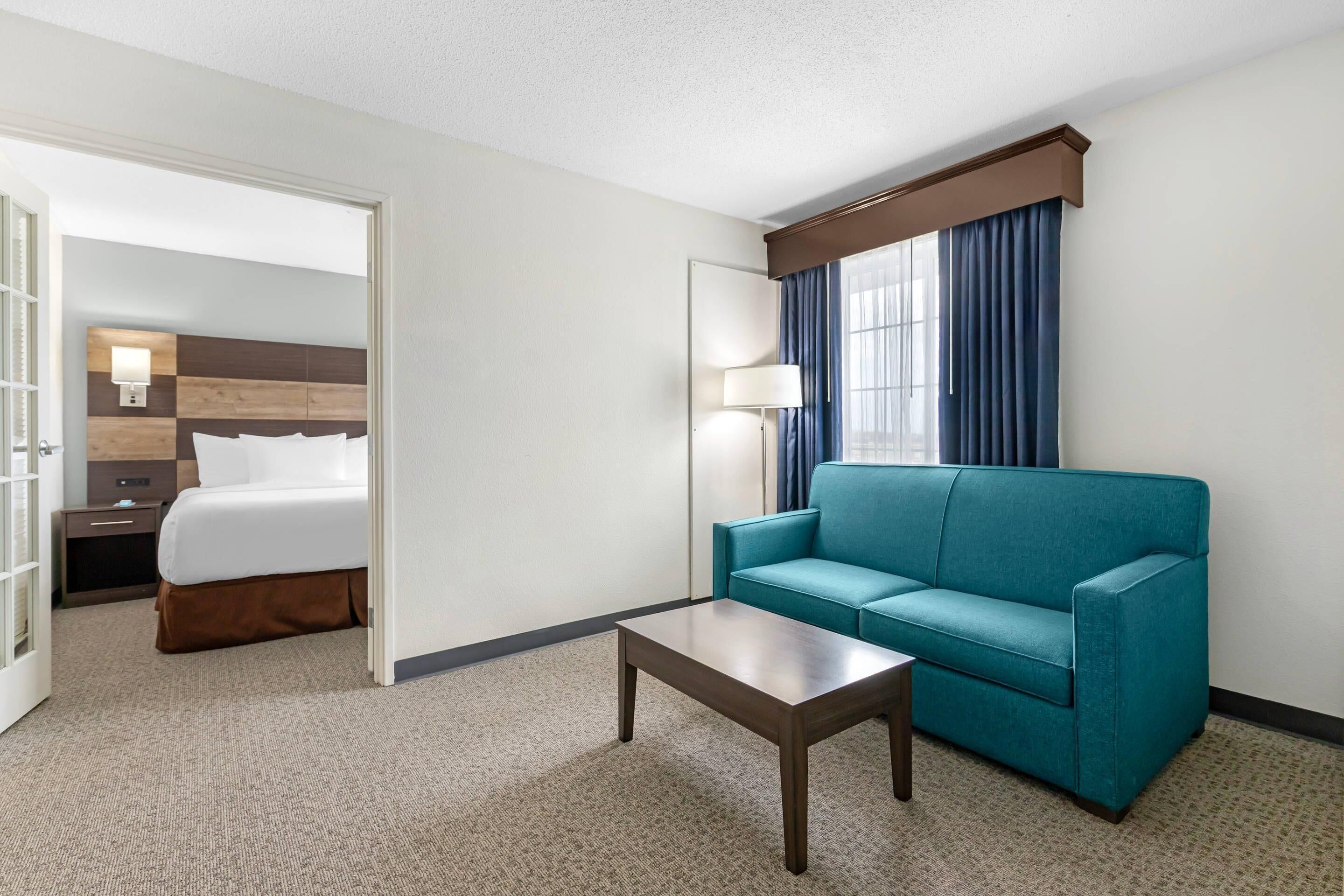Ein Hotelzimmer mit einem Bett, einem blauen Sofa, einem kleinen Tisch und einem Fenster mit Vorhängen.