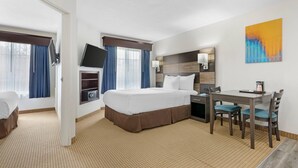 A hotel room with a bed, desk, chairs, TV, and artwork. - MainStay Suites Madison Airport (Madison)