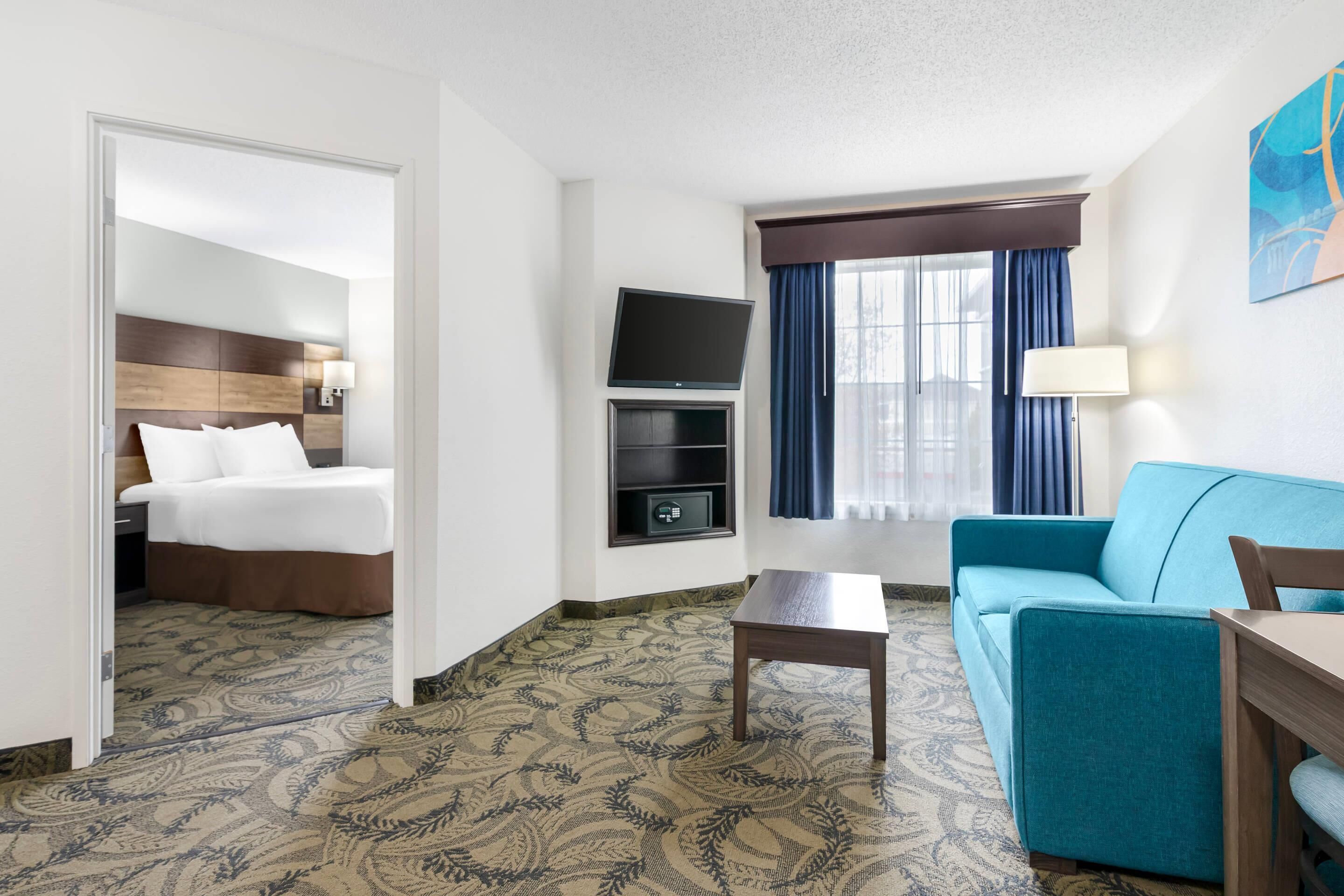 A hotel room with a bed, a TV, a sofa, a coffee table, and a patterned carpet.