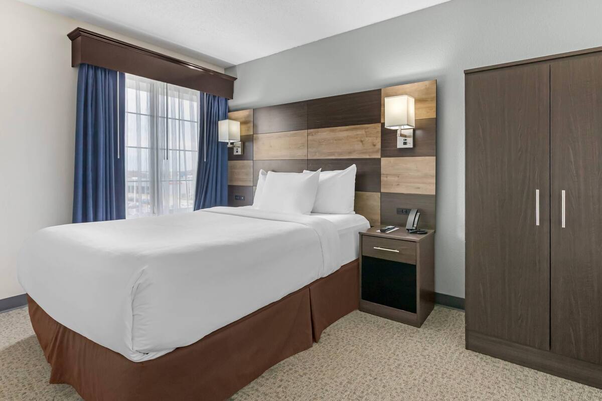 Une chambre d’hôtel avec un grand lit, une table de chevet, une armoire et une fenêtre avec des rideaux.