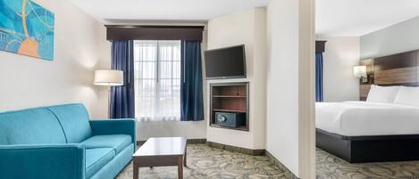 A hotel room with a teal sofa, a small table, a TV, a bed, and a patterned carpet.