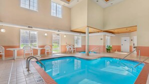 An indoor swimming pool with clear water, surrounded by white chairs and tables, and large windows allowing natural light. - MainStay Suites Madison Airport (Madison)