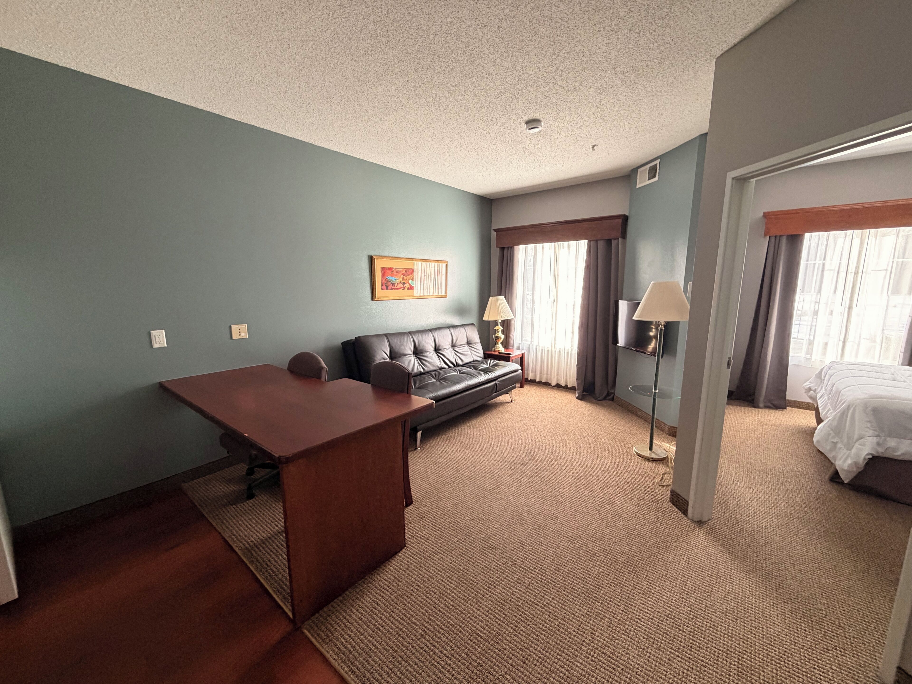 Une chambre d’hôtel avec un bureau en bois, un canapé, un lit et une télévision.