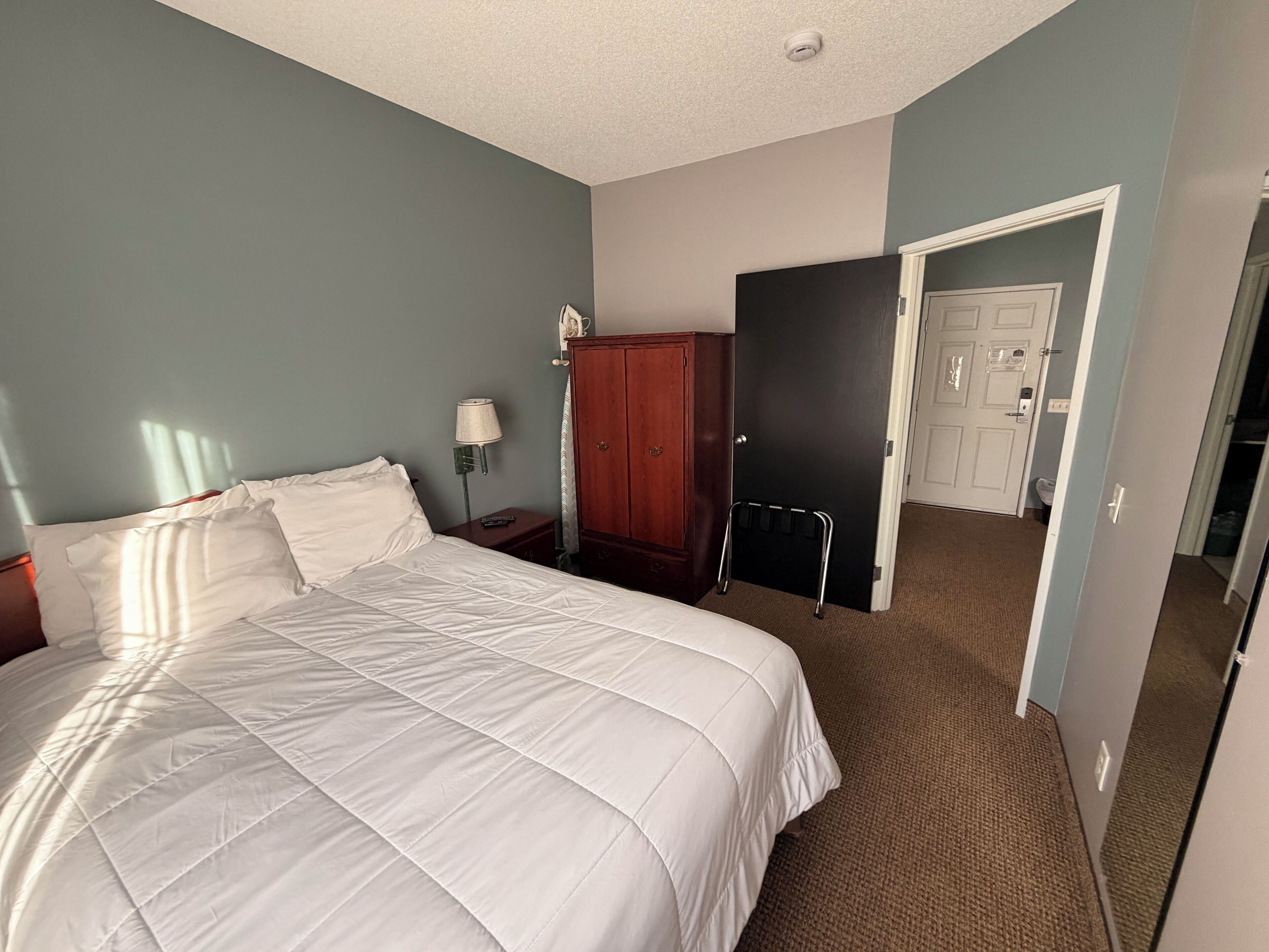Een hotelkamer met een groot bed, een kledingkast, een nachtkastje en een deur naar een badkamer.