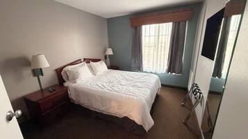 A hotel room with a large bed, two bedside tables with lamps, a window with curtains, and a door with a mirror.