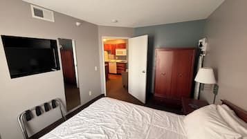 Een hotelkamer met een bed, een aan de muur bevestigde televisie, een kledingkast en een klein tafeltje met een lamp.