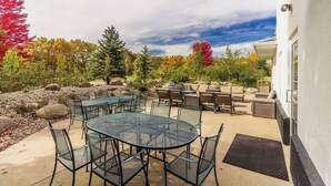 An outdoor patio with a round table and chairs, a barbecue area, and a view of trees with autumn foliage. - River Hills Hotel (Mankato)