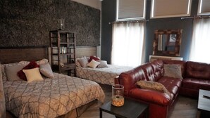 A room with two beds, a red leather sofa, a small table, and a bookshelf. - River Hills Hotel (Mankato)