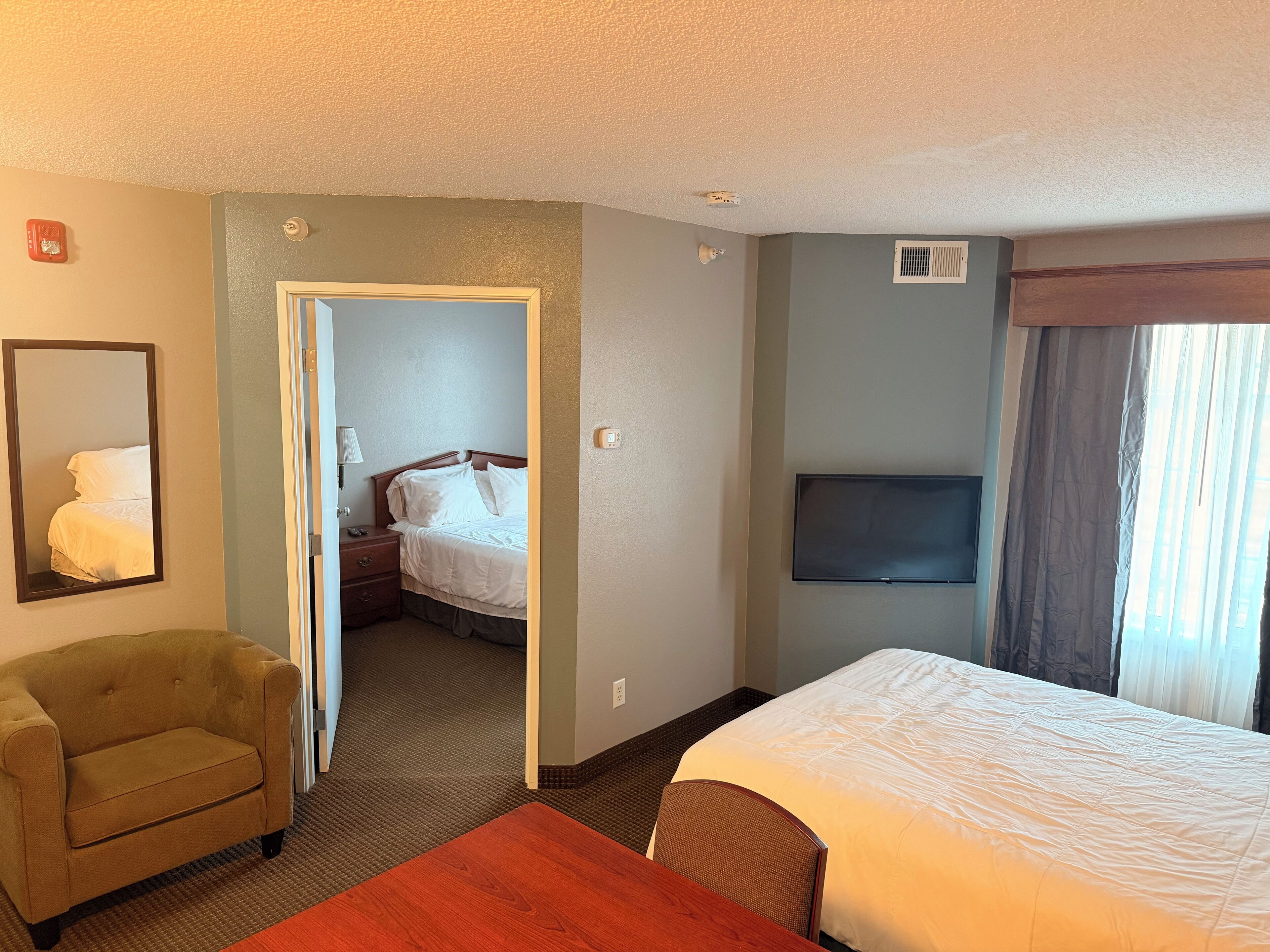 Una habitación de hotel con una cama, una silla, un televisor y una puerta que da a otra habitación.