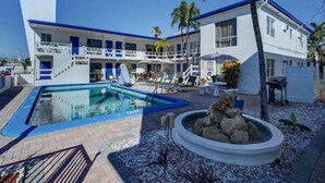 A hotel with a pool, outdoor seating, and palm trees.