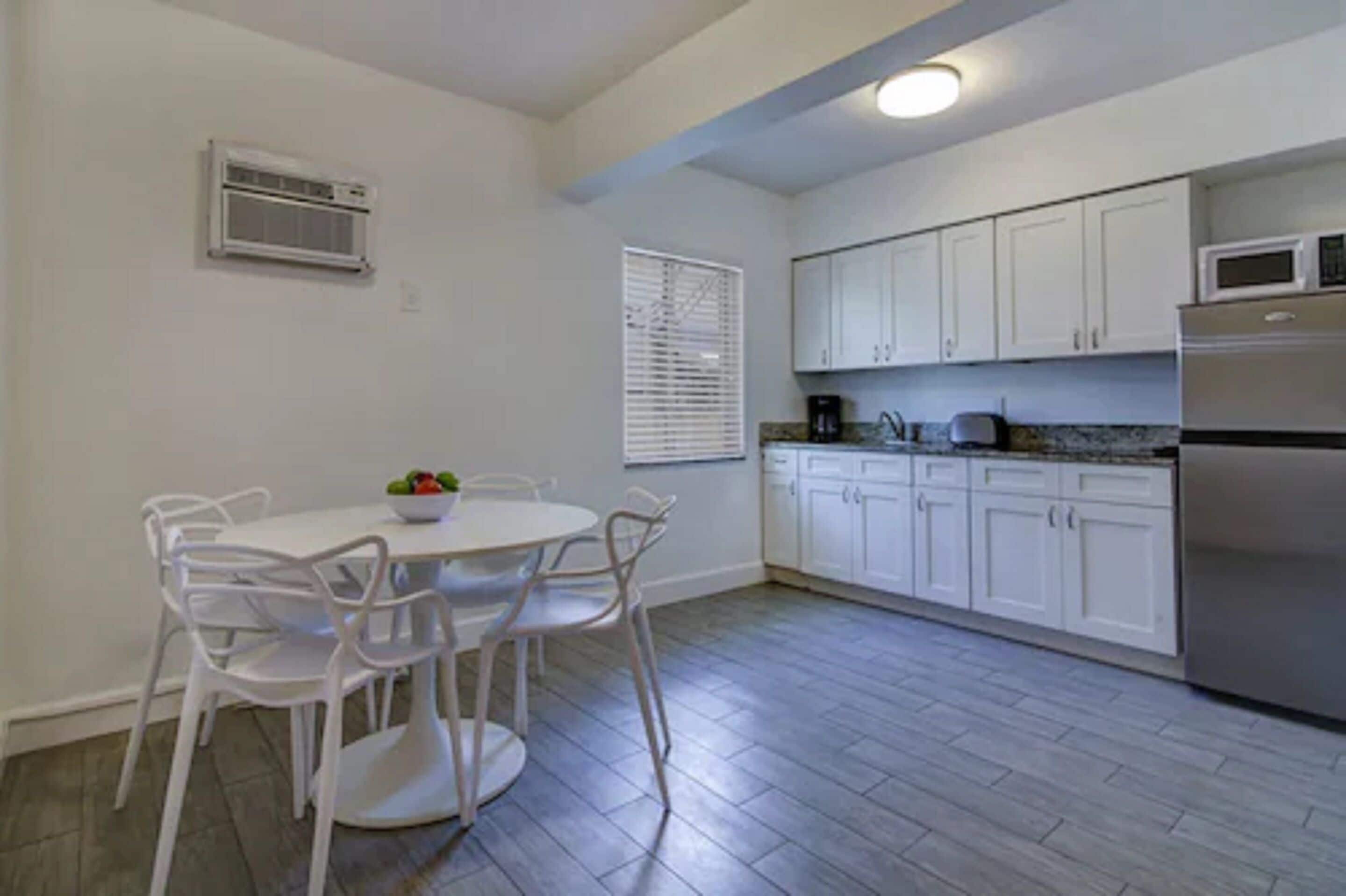 A compact kitchen with white cabinets, a stainless steel refrigerator, and a dining area with a white table and chairs.