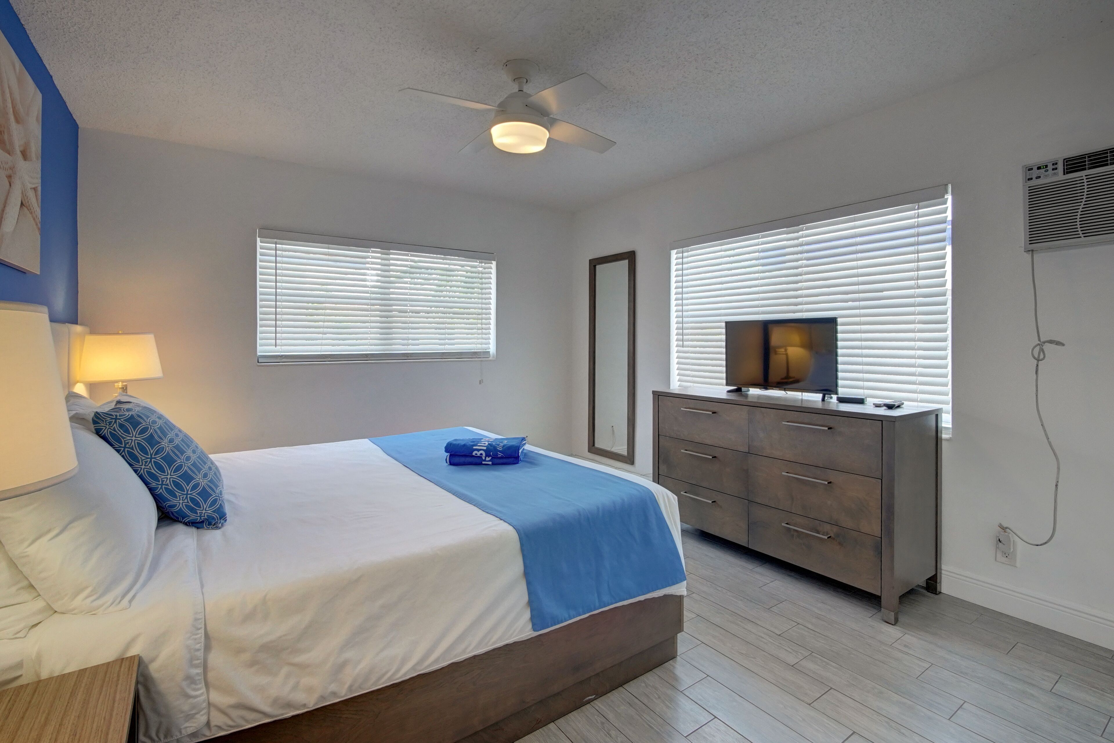 A bedroom with a bed, bedside lamp, dresser, and a ceiling fan.
