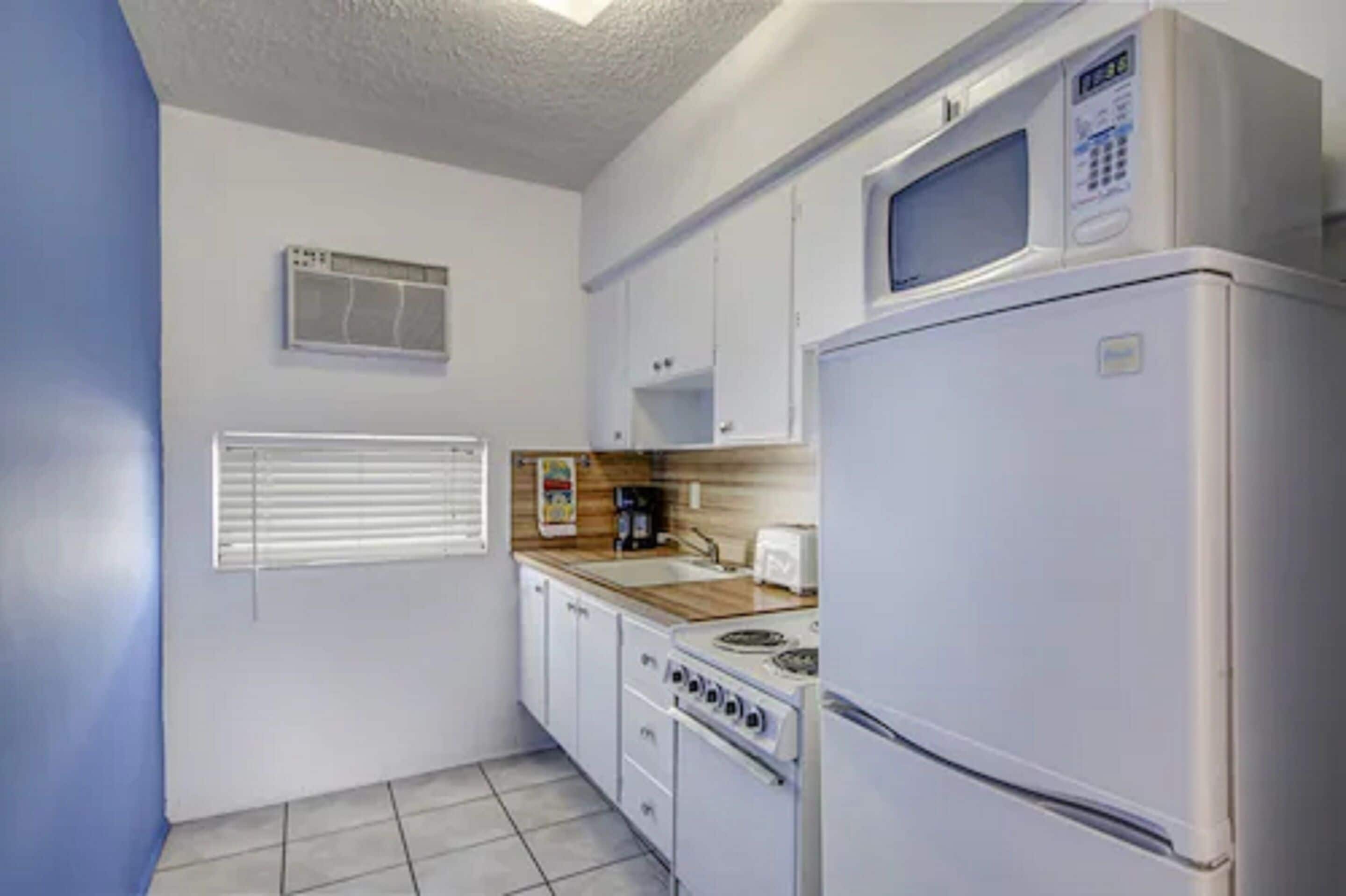 A compact kitchen with white cabinets, a microwave, a stove, and a refrigerator.