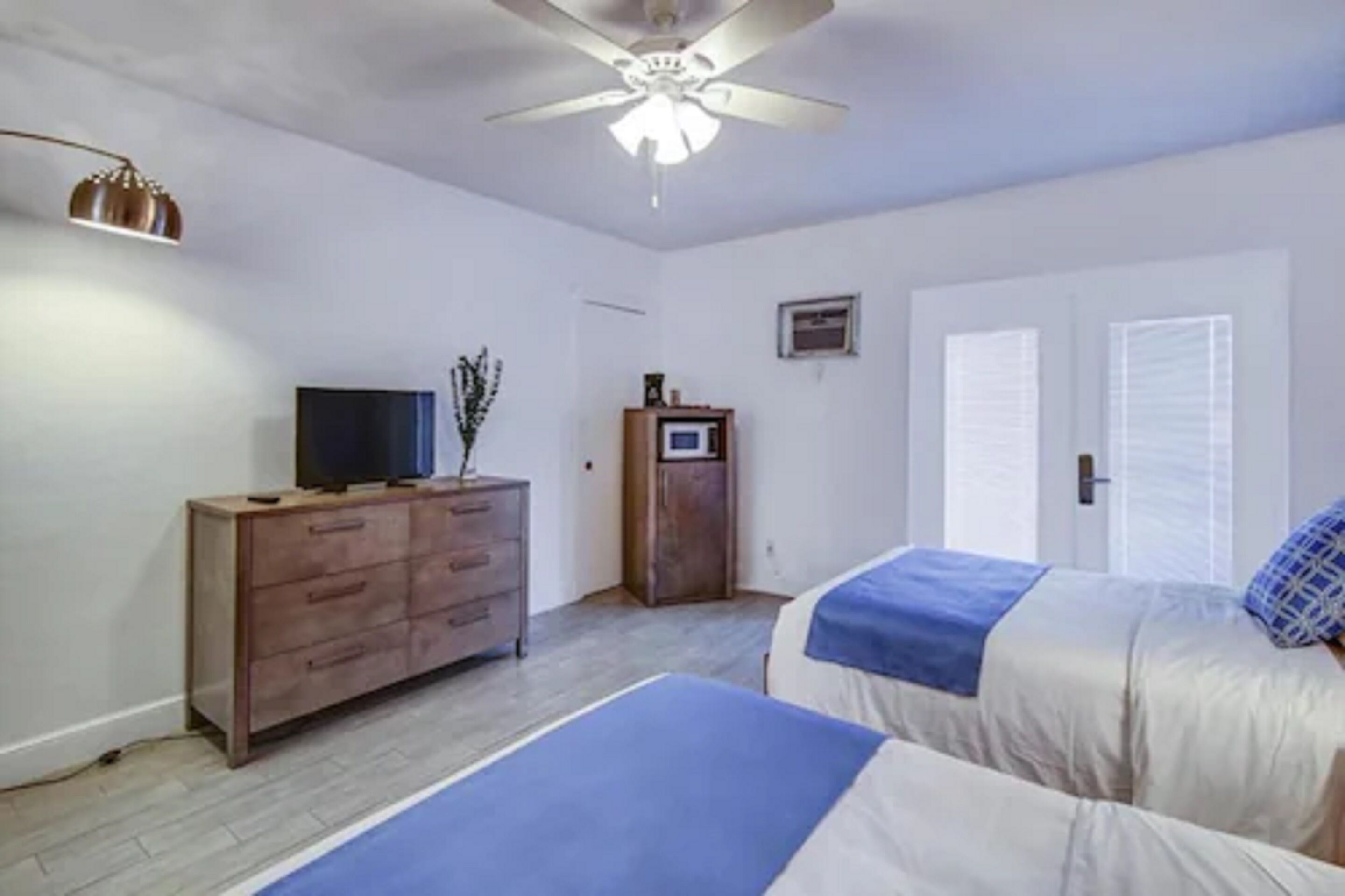 Ein Schlafzimmer mit zwei Betten, einem Deckenventilator, einem Fernseher auf einer Holzkommode und einem kleinen Schrank.