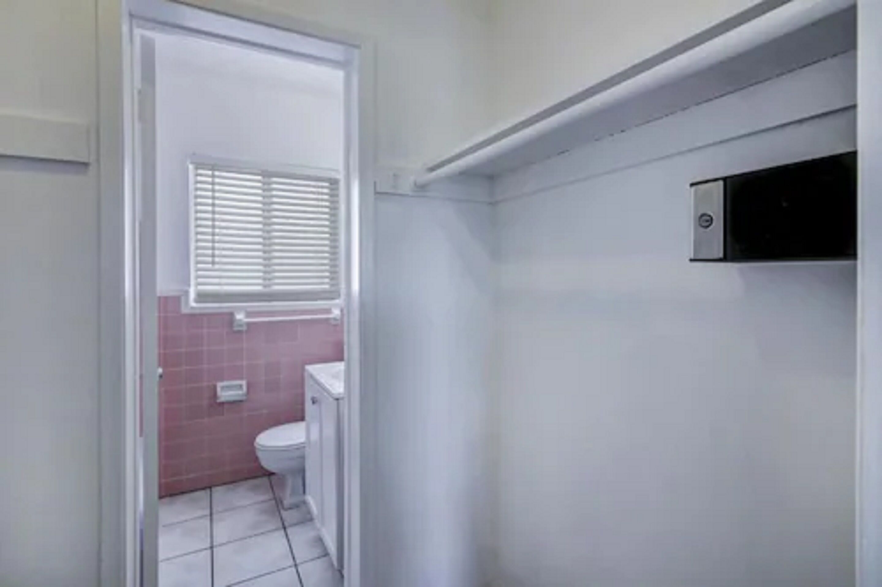 Een kleine, smalle badkamer met toilet, een raam met zonwering, en een witte wastafel.