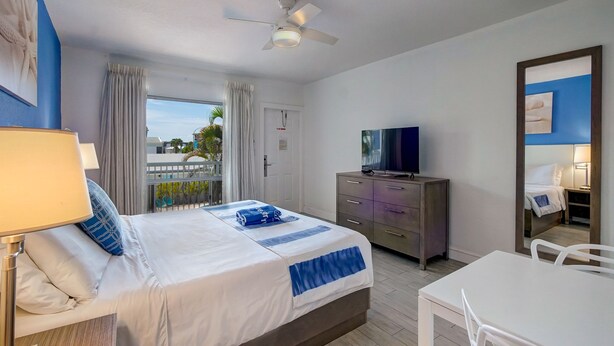 A hotel room with a bed, a desk, a TV, and a balcony with curtains.
