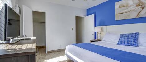 A hotel room with a bed, a desk with a computer, a ceiling fan, and a large window.