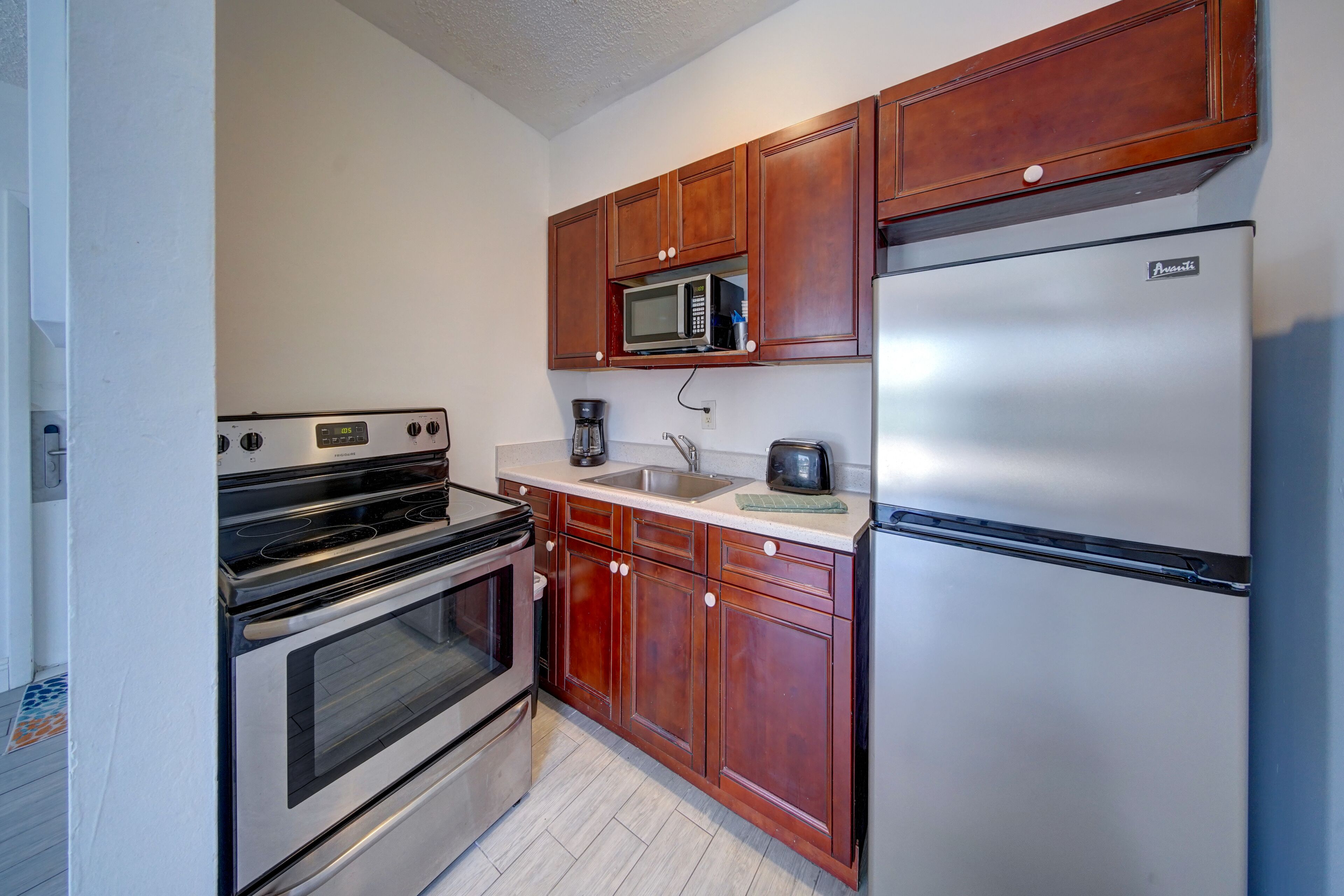 A kitchen with wooden cabinets, a stainless steel refrigerator, a microwave, a coffee maker, and an oven.