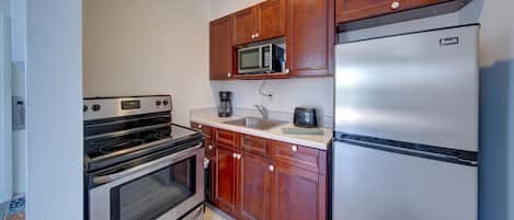 A kitchen with wooden cabinets, a stainless steel refrigerator, a microwave, a coffee maker, and an oven.