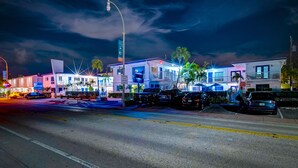 A hotel with multiple floors, a parking lot, and a street with cars and palm trees.