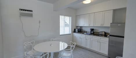 Una cocina moderna con armarios blancos, un refrigerador de acero inoxidable y una zona de comedor con sillas y una mesa blancos.