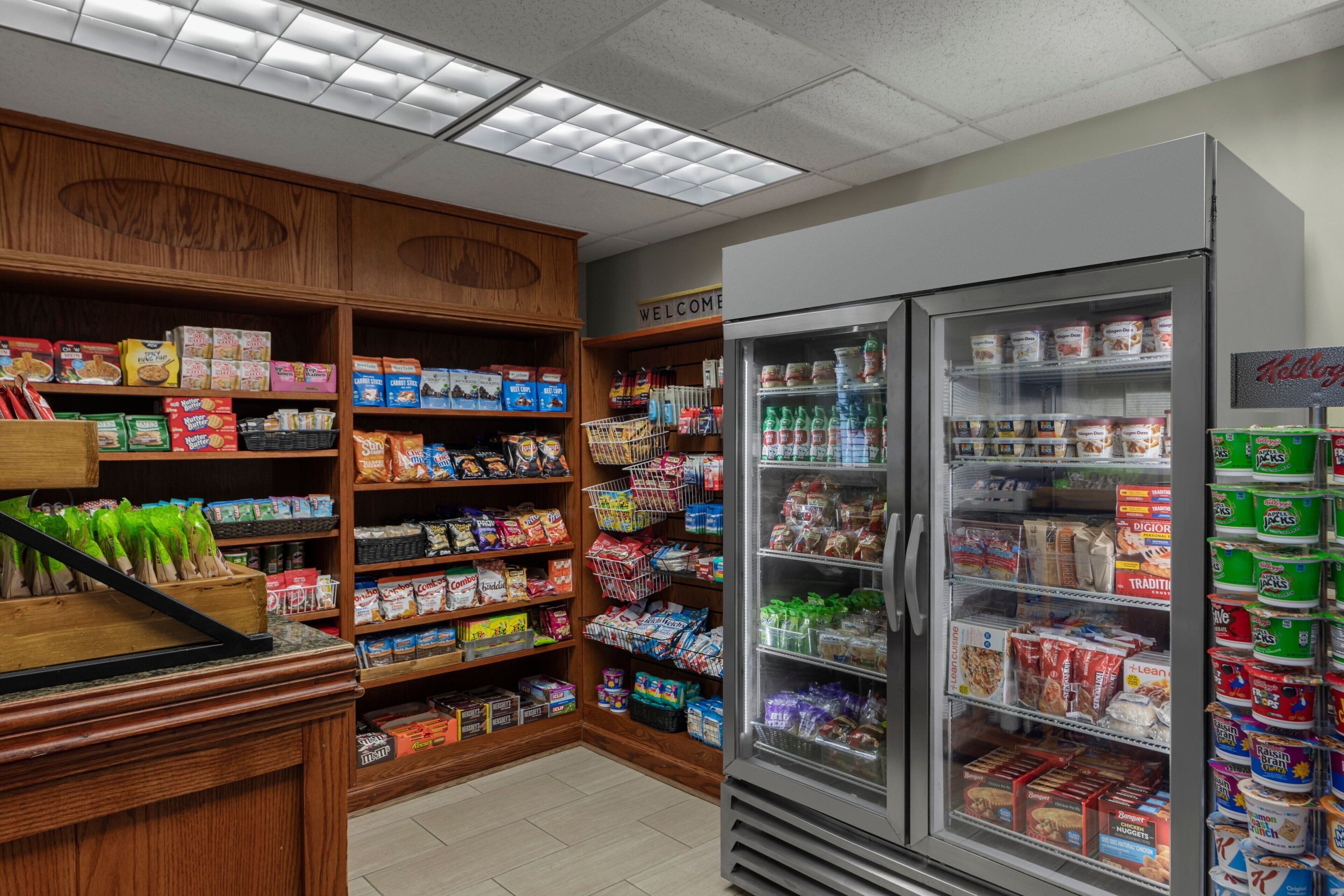 A grocery store interior with shelves stocked with various food items, a refrigerated section, and a welcome sign.