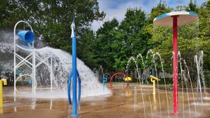 A water play area with multiple water jets and a blue and white umbrella structure.