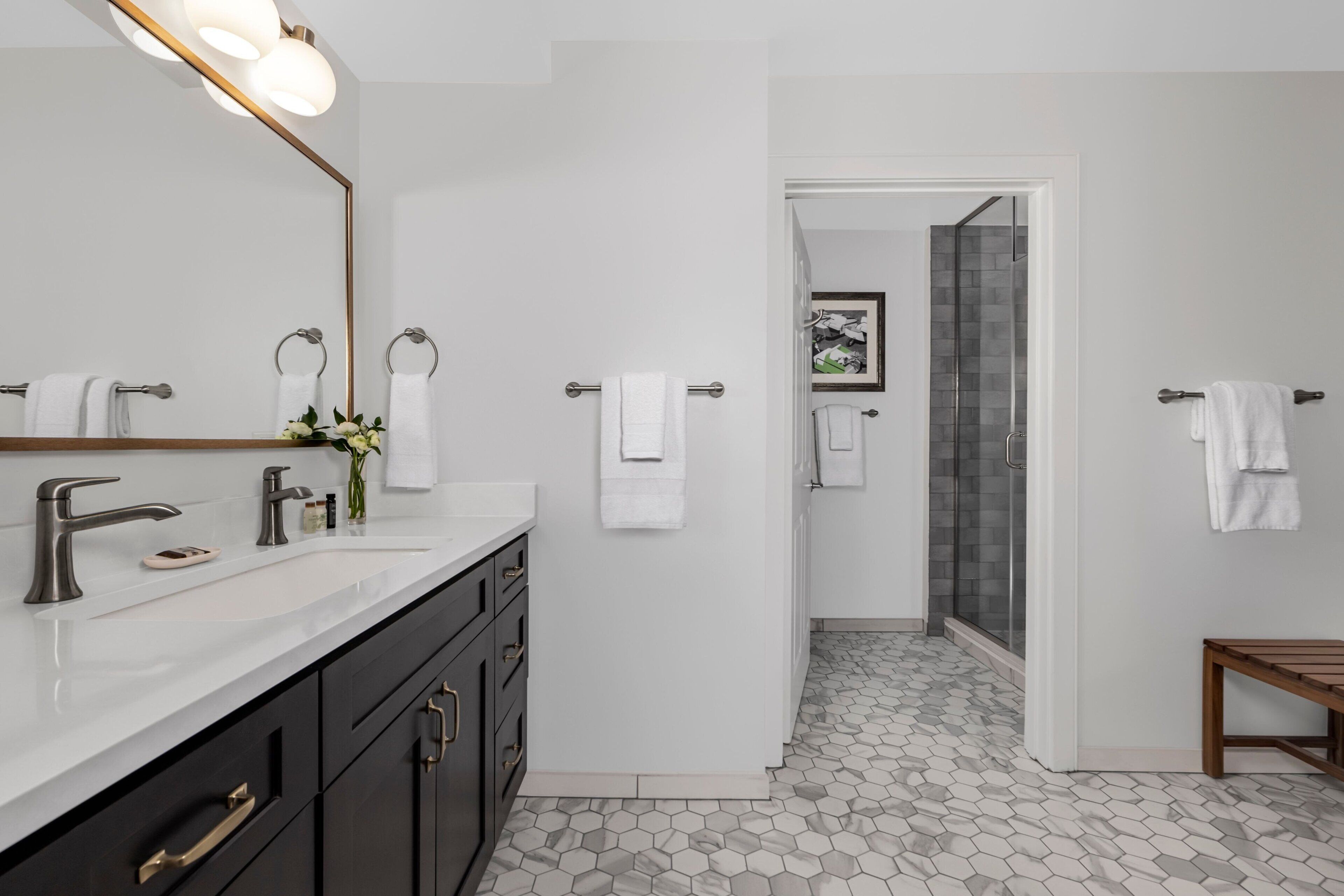A modern bathroom with a large mirror, two sinks, dark cabinets, and a shower area.