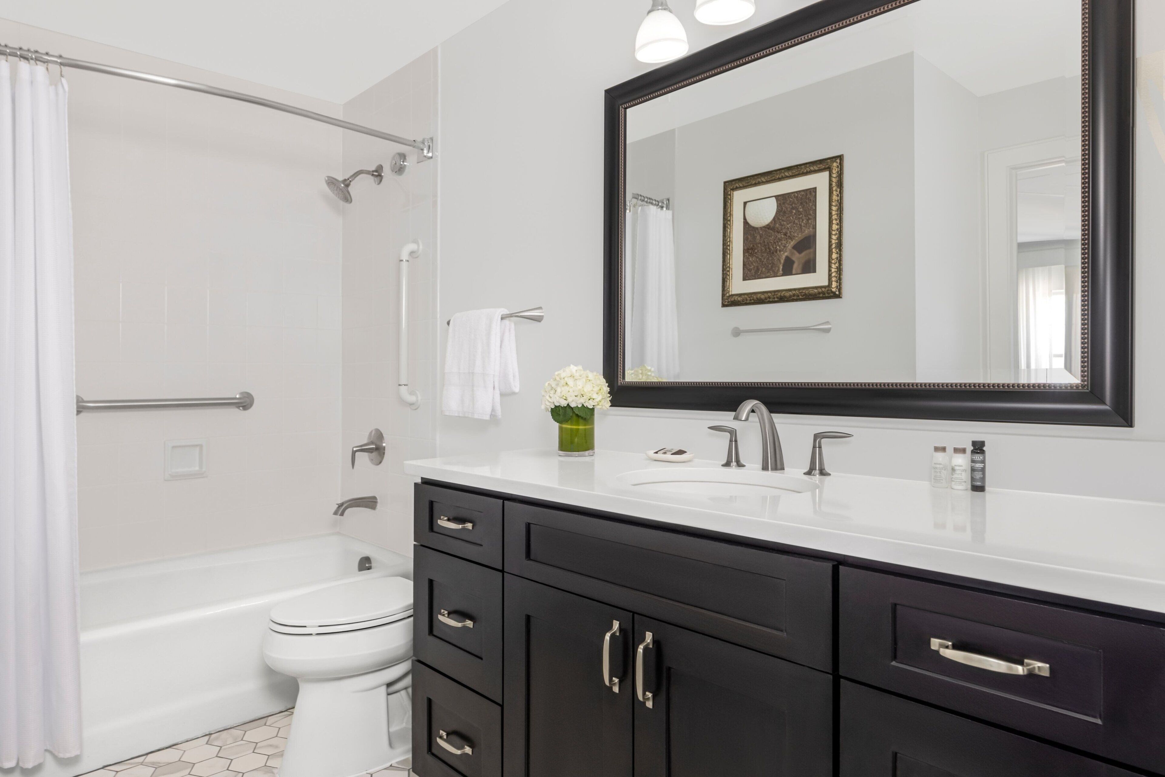 Une salle de bain moderne avec une baignoire, des toilettes, un meuble-lavabo doté de placards sombres et un grand miroir.