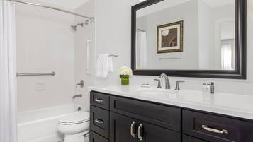 Une salle de bain moderne avec une baignoire, des toilettes, un meuble-lavabo doté de placards sombres et un grand miroir.