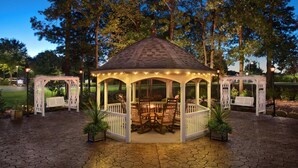 A gazebo with a tiled roof, surrounded by white railings, and furnished with wooden chairs and a table.