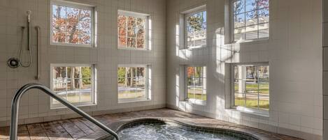 A spa area with a hot tub, large windows, and a view of trees.