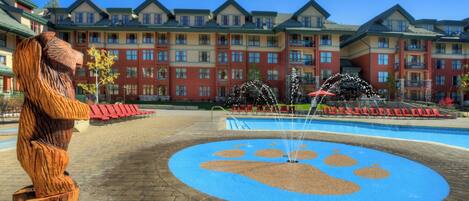 A hotel with a large outdoor pool, a wooden sculpture, and a blue paw print design on the ground.