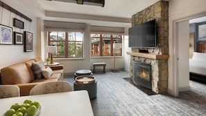 A living room with a stone fireplace, a flat-screen TV, a sofa, and a dining table with apples. - Marriott's Timber Lodge (South Lake Tahoe)