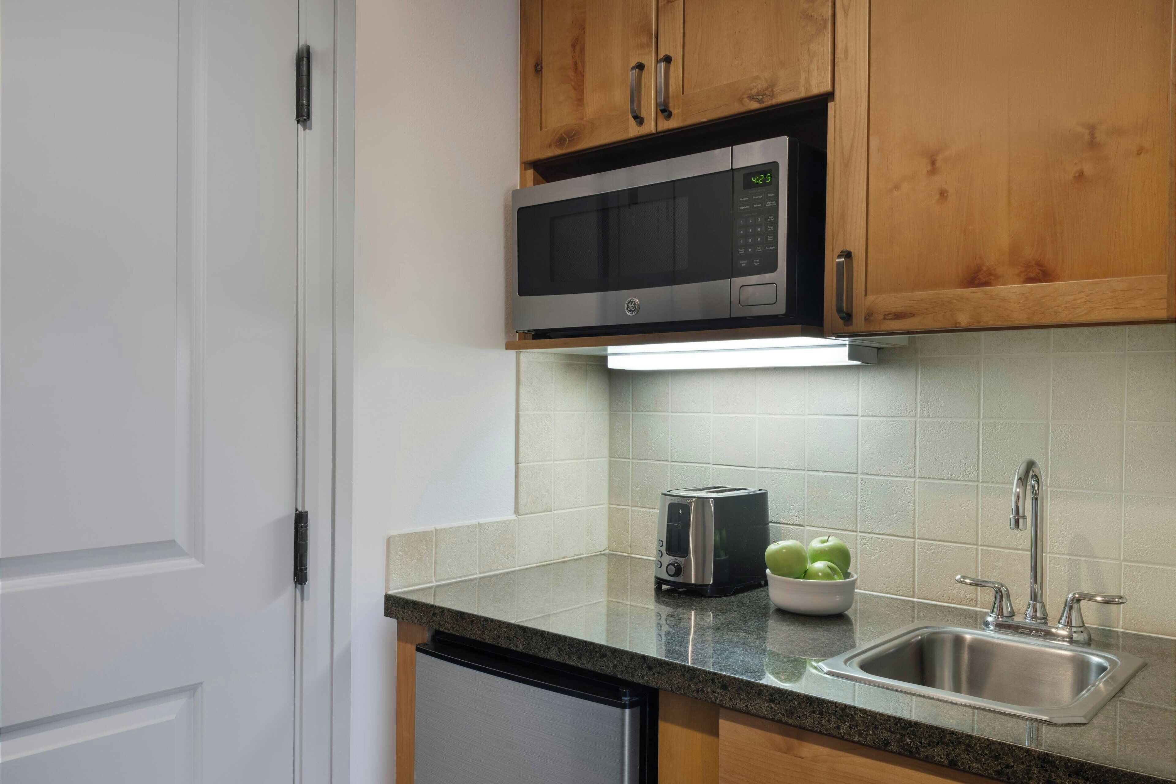 Una cocina con gabinetes de madera, un microondas de acero inoxidable, un tostador y un lavamanos.