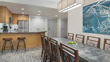 A modern kitchen with wooden cabinets, a stainless steel refrigerator, and a dining area with a long table and chairs.
