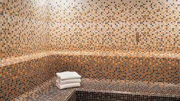 A tiled bathroom with a corner sink and a stack of white towels.