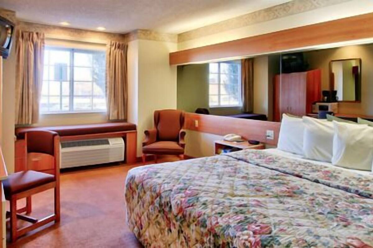 A hotel room with a bed, a desk, a chair, a TV, and a window.