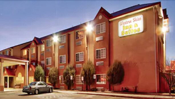 A hotel with a red facade, a gas station in front, and a sign advertising 'Western Skies Inn & Suites'. - Western Skies Inn And Suites (Los Lunas)