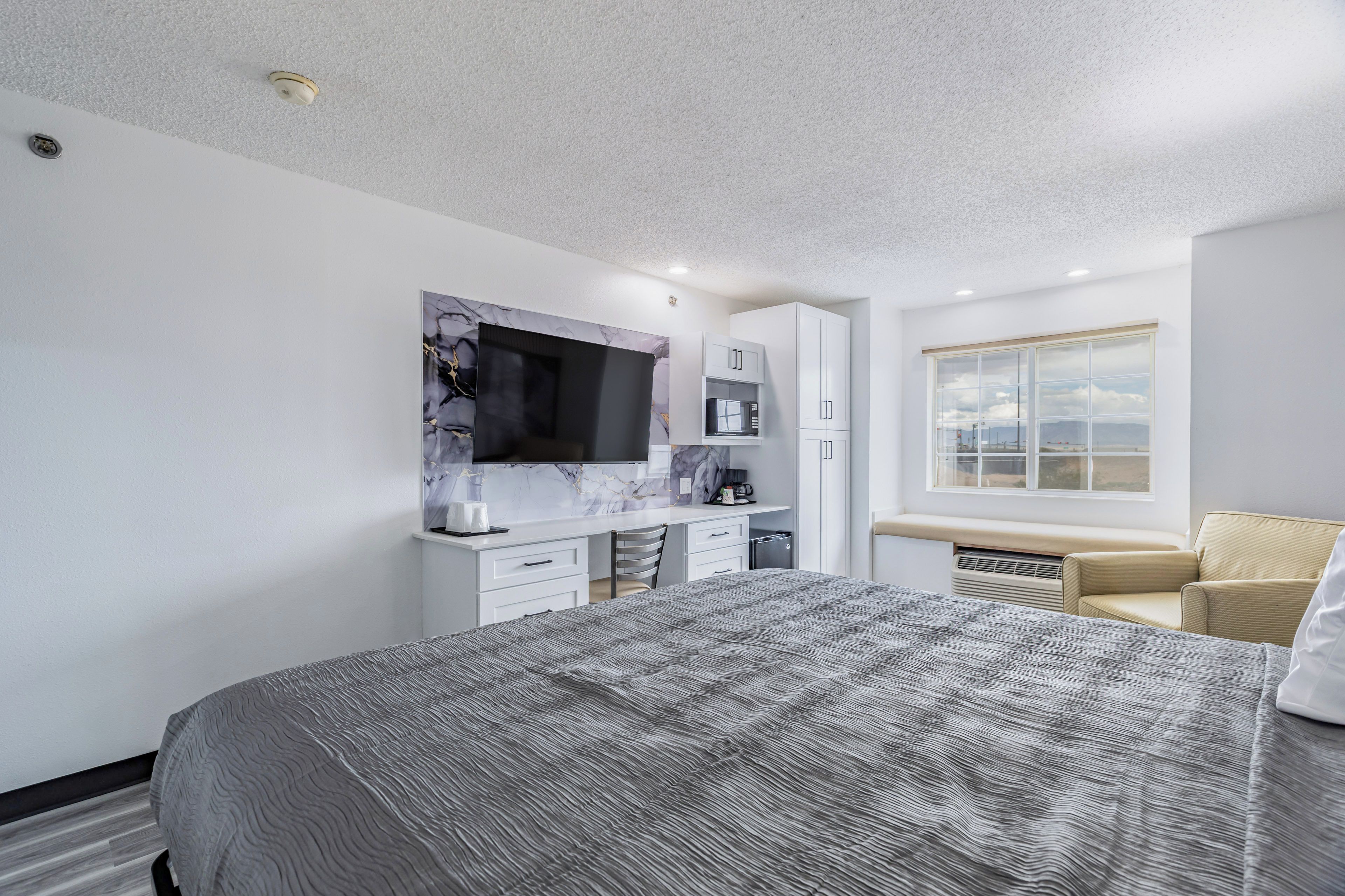 Une chambre d’hôtel moderne équipée d’un lit, d’un bureau avec un téléviseur à écran plat, d’une fenêtre donnant sur la ville et d’un radiateur intégré.