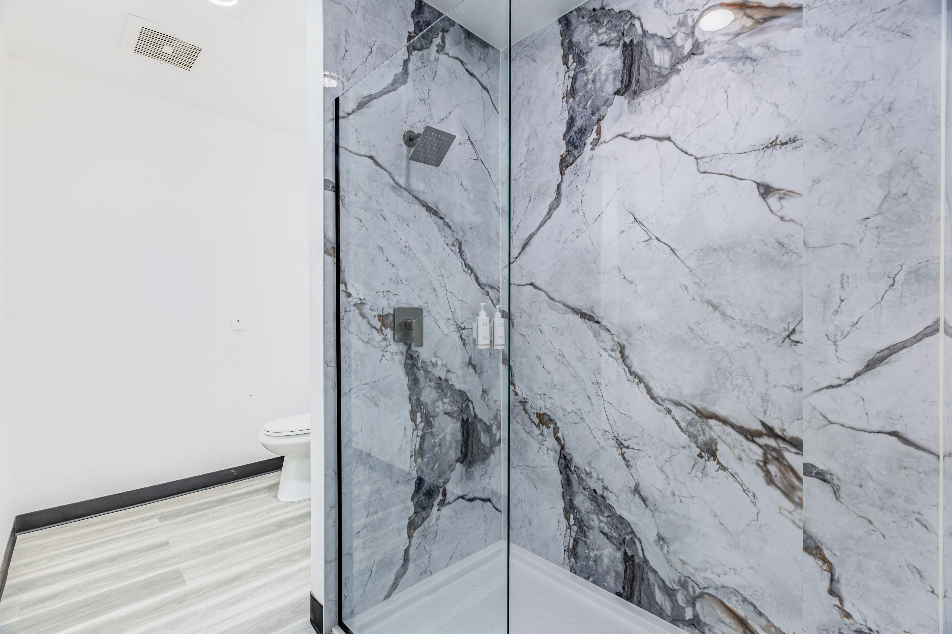 Un baño con pared de mármol, zona de ducha y un inodoro.