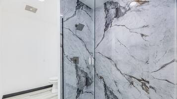 Un baño con pared de mármol, zona de ducha y un inodoro.