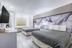 Quarto de hotel com duas camas, televisão de tela plana, máquina de café e cabeceira com padrão marmorizado.