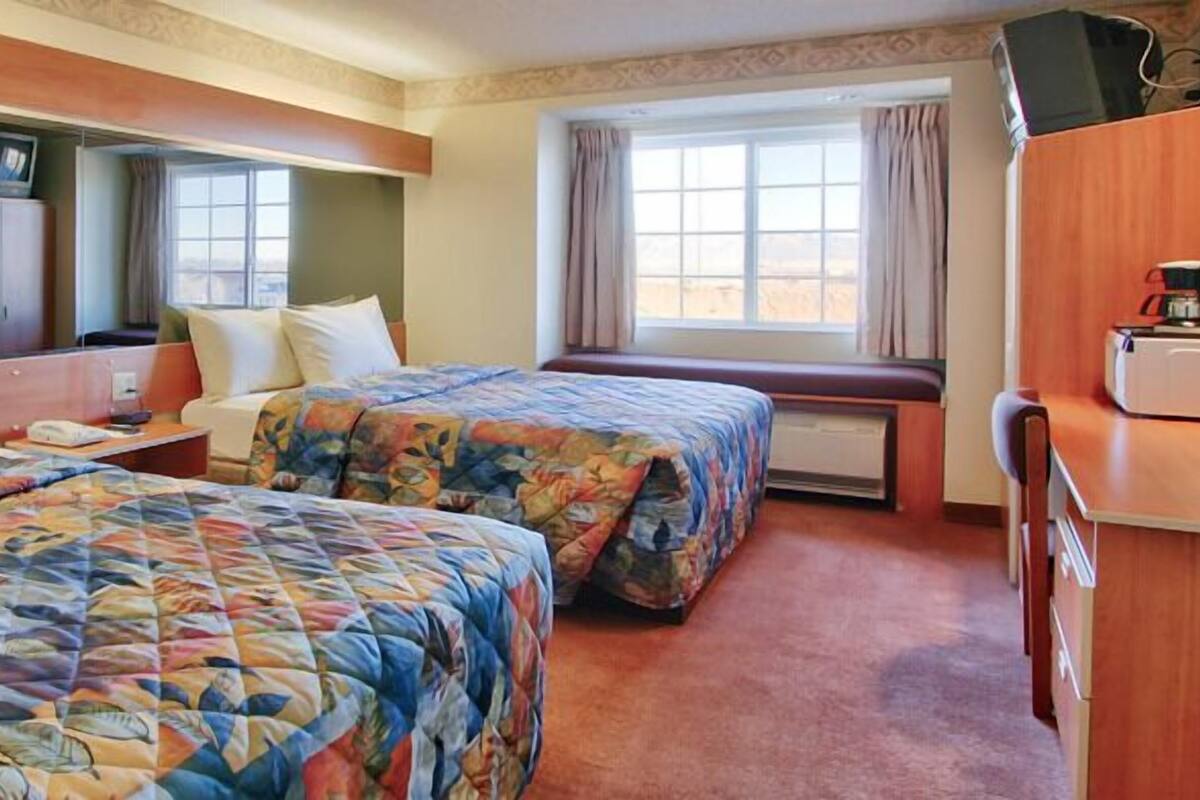 A hotel room with two beds, a television, a desk, and a window with curtains.