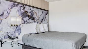 Una habitación de hotel moderna con cabecera de diseño de mármol, mesita de noche con lámpara y colcha gris.