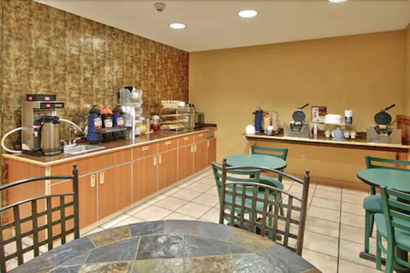 A hotel breakfast area with a coffee station, seating, and a tiled floor. - Western Skies Inn And Suites (Los Lunas)