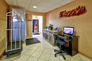 A hotel lobby with a reception desk, computer, and a metal cart. - Western Skies Inn And Suites (Los Lunas)