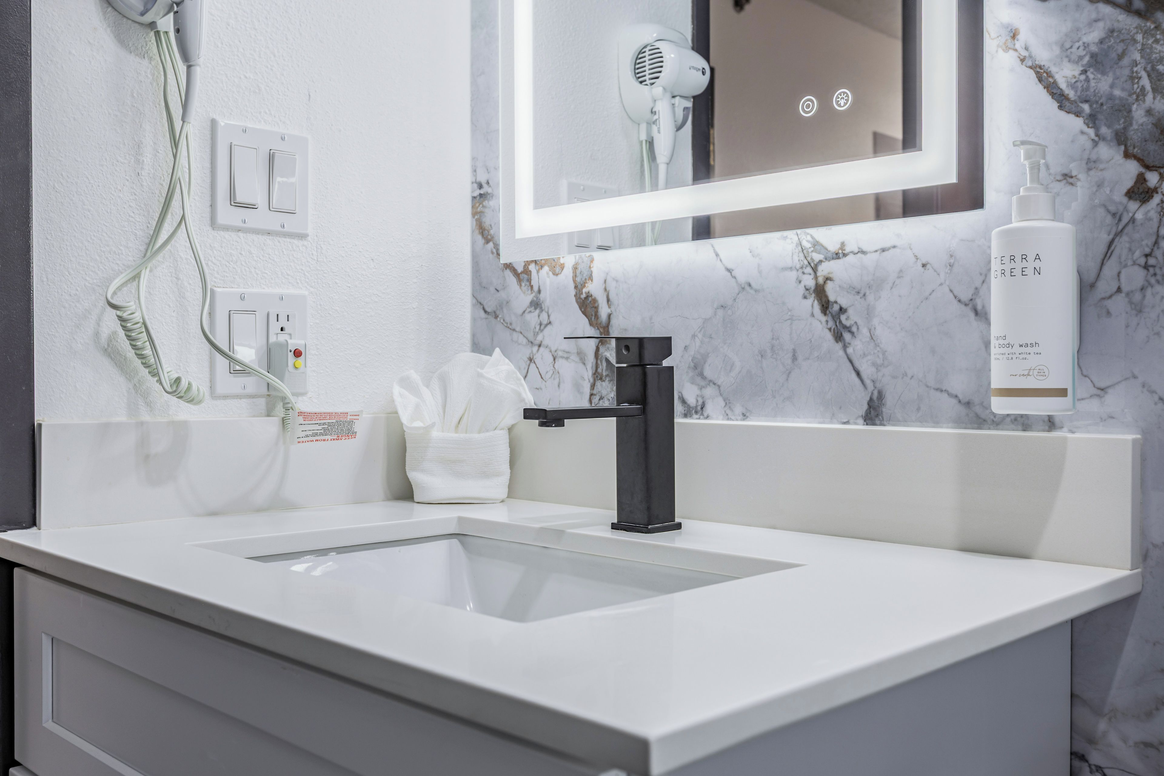 A modern bathroom with a white sink, a black faucet, a towel dispenser, and a hand soap bottle.